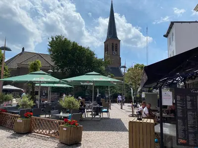 a street with tables and umbrellas and a clock tower at @54 in Zandvoort