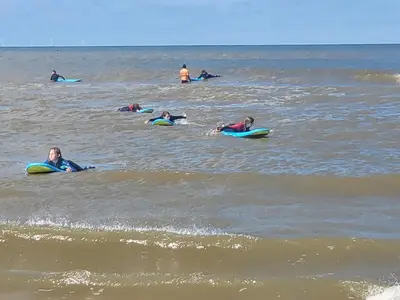 a group of people laying on surfboards in the ocean at Appartement Canberra. in Bergen aan Zee