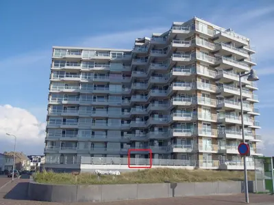 a tall apartment building with a red sign in front of it at Sterflat 45 in Egmond aan Zee