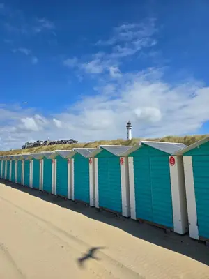 a row of blue beach huts on a beach with a lighthouse at Beach 44 in Egmond aan Zee