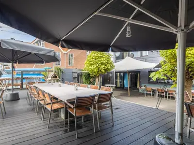 a table with chairs and an umbrella on a deck at De Kaag Watersport Groepsaccommodatie - 30 pers in Kaag