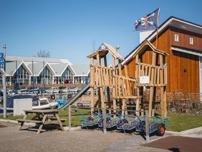 a wooden playground with a slide in front of a marina at Spacious Lakeside Retreat in Uitgeest