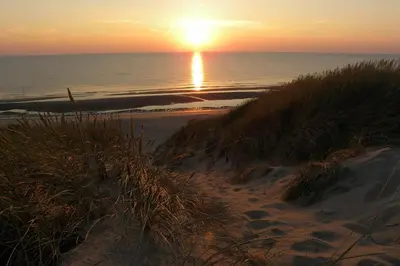 a sunset on a beach with the ocean and the sand at Dune Lagoon in Egmond aan den Hoef