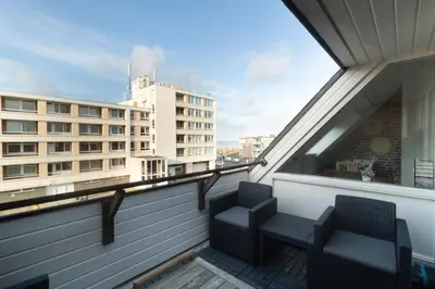 two chairs on a balcony with a view of a building at Strand appartement aan zee met 2 parkeerplekken! in Egmond aan Zee