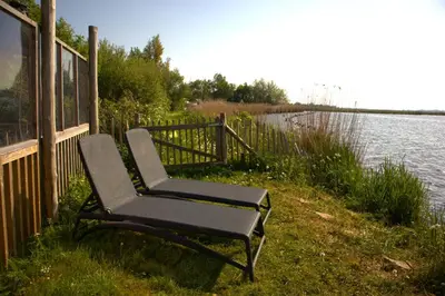 a chair sitting next to a fence next to a body of water at Glampingtent de Saskerlei, de Woudhaven in De Woude