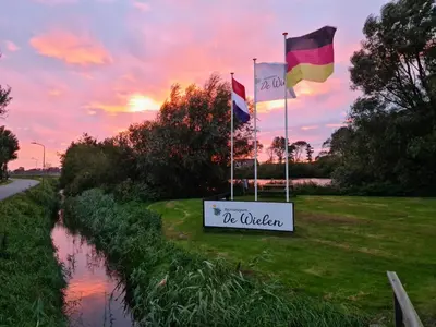 three flags on the side of a river with a sign at Chalet 588 op Recreatiepark De Wielen in Sint Maarten