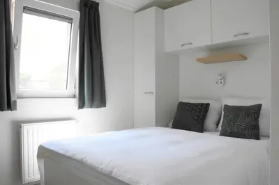 a bedroom with a white bed and a window at Recreatie aan de Vecht, chalet 3, genieten van de rust en ruimte en toch dichtbij de stad in Weesp