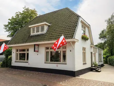 a small white house with red and white flags on it at Holiday Home in Bergen near Bergerbos Forest in Bergen