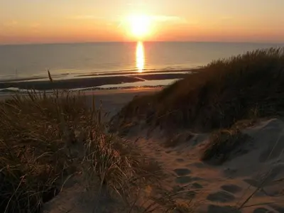 a sunset on a beach with the ocean and the sand at Holiday Home in Bergen near Bergerbos Forest in Bergen