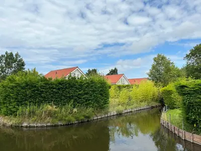 a river with bushes and houses in the background at Holiday Home Alk 8-2 by Interhome in Noordwijkerhout