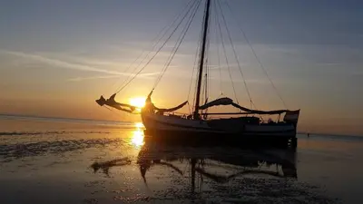 a boat sitting on the beach at sunset at Tjalkjacht Pelikaan Volendam in Volendam
