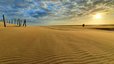 a person standing on a sandy beach with the sunset at Hotel de Baak Seaside in Noordwijk aan Zee