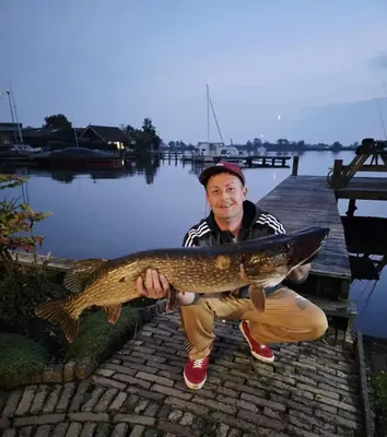 a man holding a fish in front of a dock at Vakantie huis aan het water in Rijpwetering