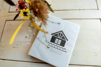 a white card with a house on it next to flowers at klein polderhuis - bollenschuur in Roelofarendsveen