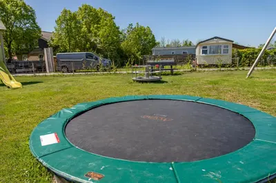 a circular trampoline in a yard with a playground at Chalet 575 op Recreatiepark De Wielen in Sint Maarten
