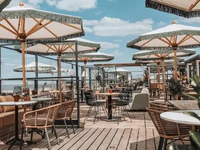 an outdoor patio with tables and chairs and umbrellas at La Siesta Noordwijk Zee in Noordwijk
