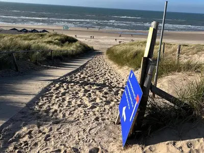 a blue sign in the sand on a beach at Studio aan Zee op 150 Meter van Strand in Egmond aan Zee